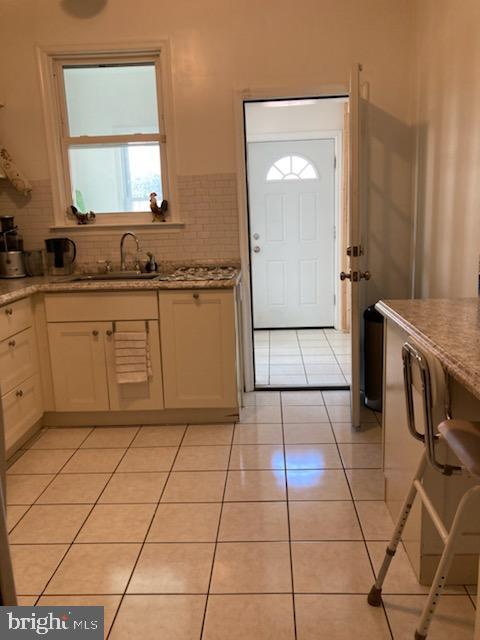 kitchen featuring sink, light stone counters, tasteful backsplash, and light tile flooring