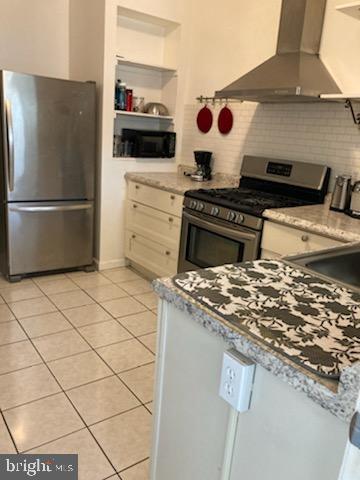 kitchen featuring light stone countertops, backsplash, stainless steel appliances, light tile floors, and wall chimney exhaust hood