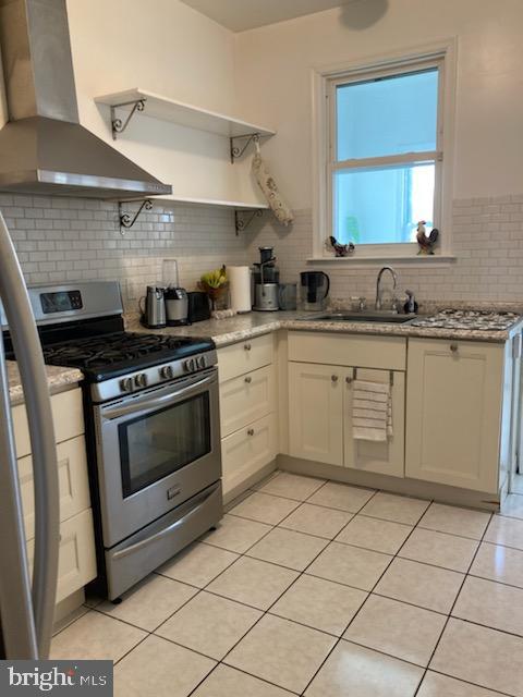 kitchen featuring tasteful backsplash, gas stove, light tile floors, and wall chimney range hood