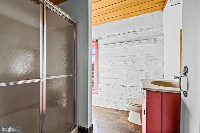 bathroom featuring brick wall, toilet, a shower with shower door, vanity, and hardwood / wood-style floors