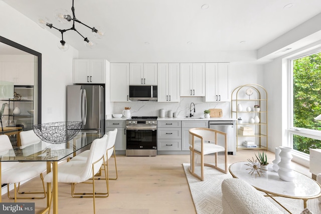 kitchen with light hardwood / wood-style flooring, appliances with stainless steel finishes, tasteful backsplash, plenty of natural light, and white cabinetry