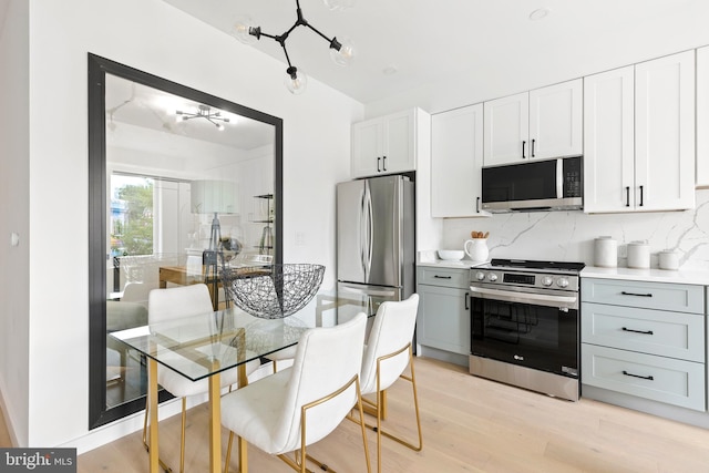 kitchen with appliances with stainless steel finishes, tasteful backsplash, gray cabinetry, light hardwood / wood-style floors, and white cabinetry