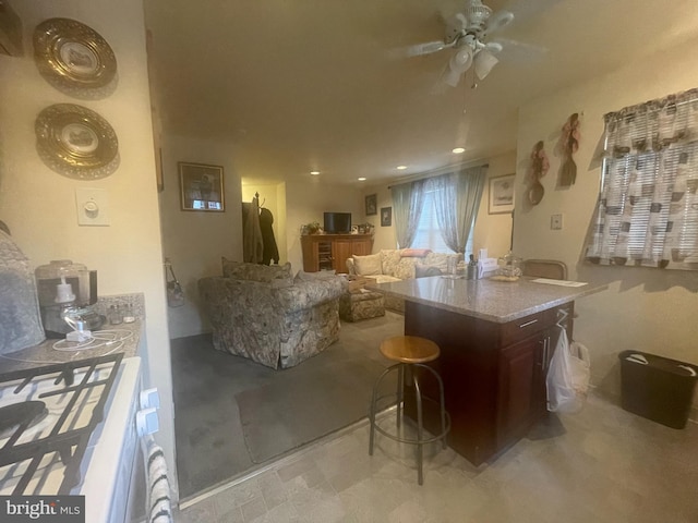 kitchen featuring ceiling fan, dark brown cabinets, a breakfast bar area, and light stone countertops