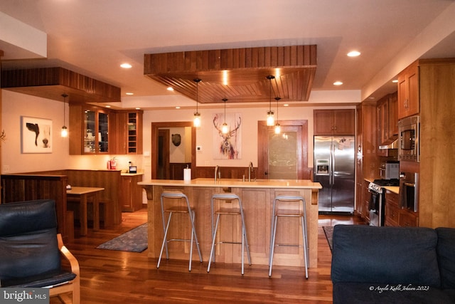 kitchen with hanging light fixtures, a center island, dark wood-type flooring, stainless steel appliances, and a kitchen bar