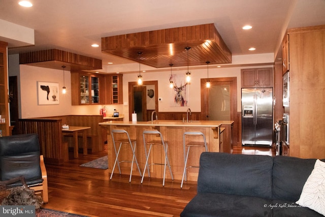 kitchen featuring refrigerator, a breakfast bar, wall oven, dark wood-type flooring, and hanging light fixtures