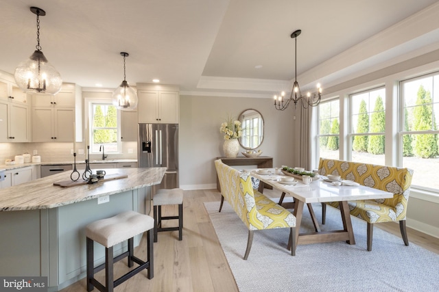 dining area with a chandelier, sink, a tray ceiling, and light hardwood / wood-style floors