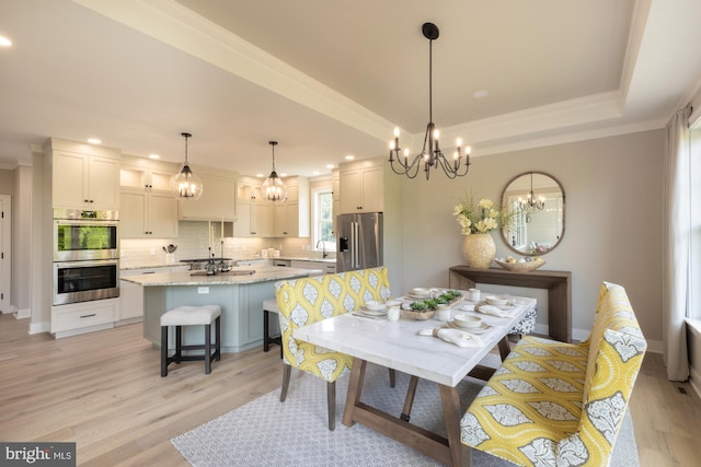 dining area with an inviting chandelier, sink, a tray ceiling, and light hardwood / wood-style floors