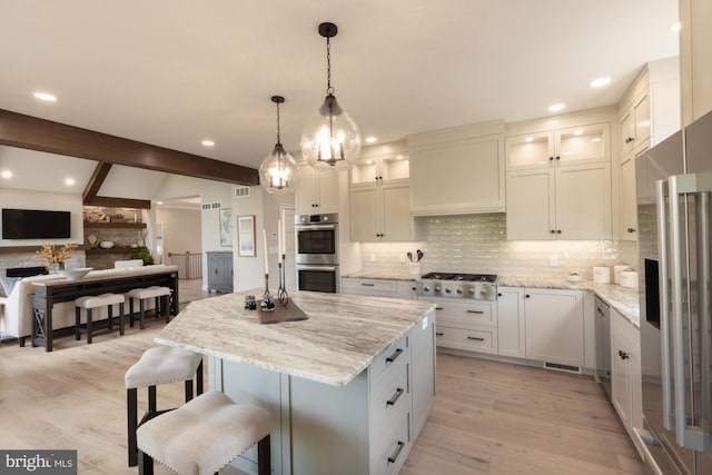 kitchen featuring a kitchen bar, appliances with stainless steel finishes, light hardwood / wood-style flooring, a center island, and light stone counters