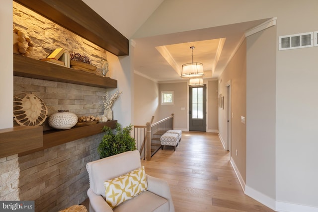 foyer with ornamental molding, a raised ceiling, and light hardwood / wood-style flooring