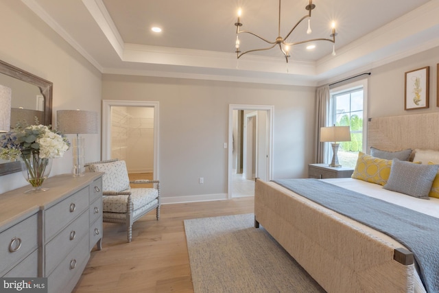 bedroom with a spacious closet, a raised ceiling, a chandelier, and light hardwood / wood-style floors