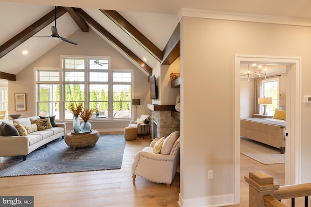 living room with ceiling fan with notable chandelier, high vaulted ceiling, a brick fireplace, light hardwood / wood-style flooring, and beam ceiling