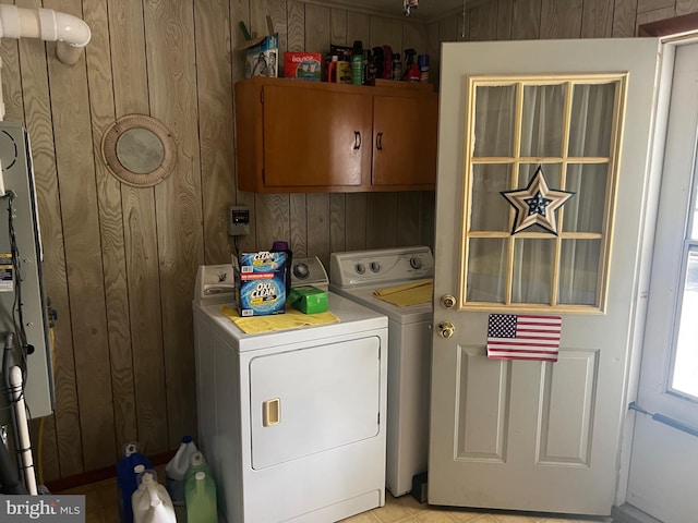 laundry area with wood walls, washer and clothes dryer, and cabinets