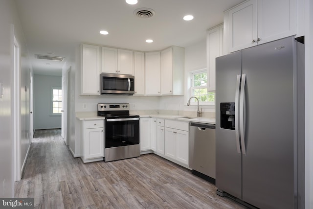 kitchen with white cabinetry, stainless steel appliances, sink, and light hardwood / wood-style flooring