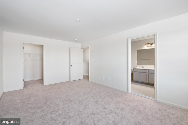 unfurnished bedroom with light colored carpet, sink, a spacious closet, ensuite bathroom, and a closet