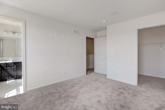 unfurnished bedroom with light carpet and a walk in closet