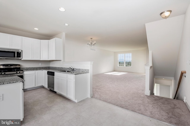 kitchen with appliances with stainless steel finishes, white cabinetry, dark stone countertops, a notable chandelier, and sink