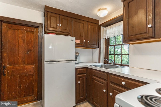 kitchen featuring sink, white refrigerator, light tile floors, and stove