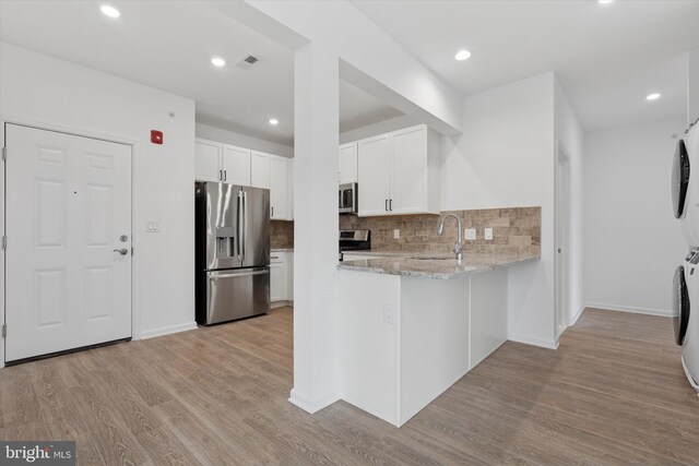 16231 River View Dr, Bristol, PA 19007 - kitchen with appliances with stainless steel finishes, stacked washing machine and dryer, light stone countertops, tasteful backsplash, and light wood-style floors