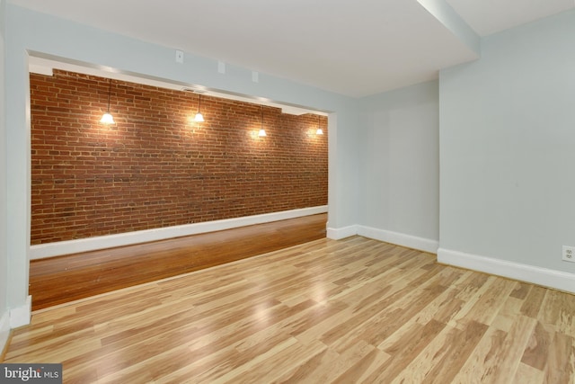 empty room featuring brick wall and light hardwood / wood-style floors