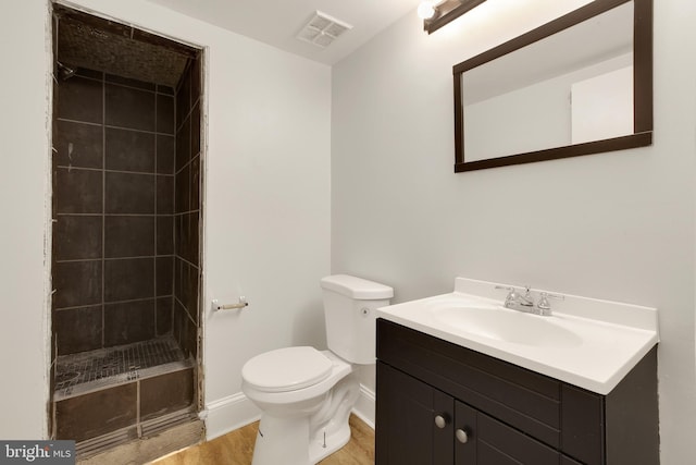 bathroom featuring large vanity, toilet, a tile shower, and wood-type flooring