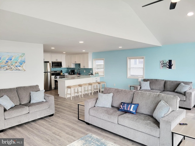 living room featuring light hardwood / wood-style flooring, ceiling fan, sink, and high vaulted ceiling