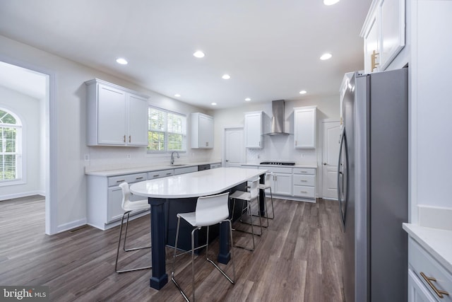 kitchen featuring wall chimney exhaust hood, a kitchen breakfast bar, white cabinets, and stainless steel refrigerator