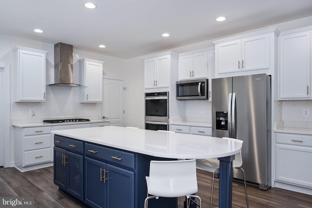 kitchen featuring appliances with stainless steel finishes, blue cabinets, wall chimney exhaust hood, white cabinets, and dark wood-type flooring