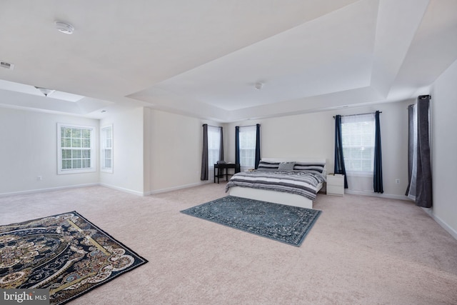 bedroom with multiple windows, light colored carpet, and a raised ceiling