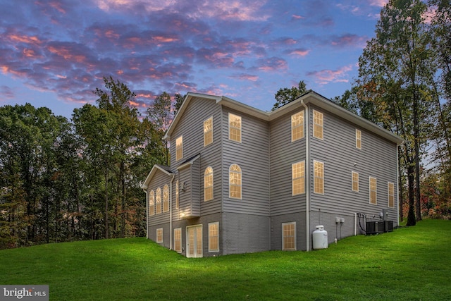 property exterior at dusk with central AC and a lawn