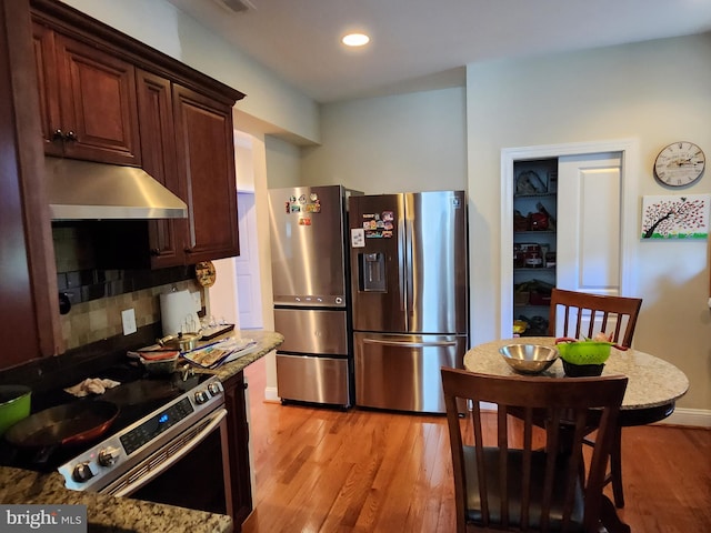 kitchen featuring appliances with stainless steel finishes, light wood-type flooring, light stone counters, backsplash, and dark brown cabinetry