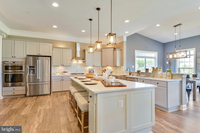 kitchen with a kitchen island, hanging light fixtures, stainless steel appliances, wall chimney exhaust hood, and a kitchen bar