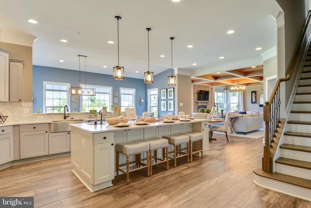 kitchen featuring coffered ceiling, hanging light fixtures, a kitchen bar, a kitchen island with sink, and sink