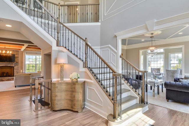 stairs with coffered ceiling, a notable chandelier, beam ceiling, a stone fireplace, and light hardwood / wood-style flooring