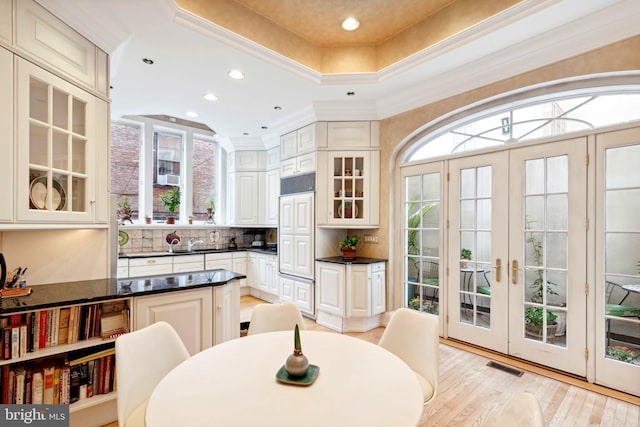 dining room with light hardwood / wood-style floors, french doors, crown molding, a raised ceiling, and sink