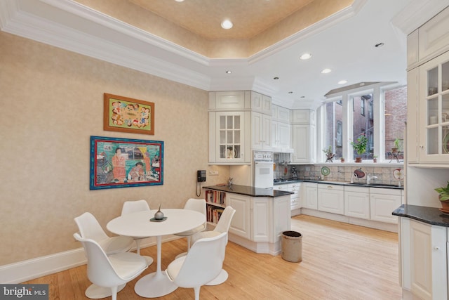 kitchen featuring oven, crown molding, light hardwood / wood-style floors, tasteful backsplash, and white cabinetry