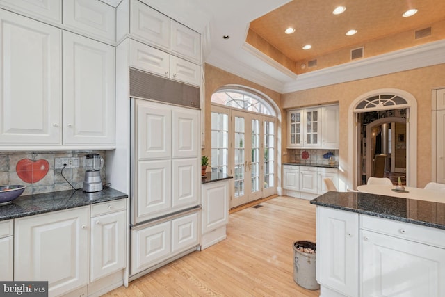 kitchen featuring light hardwood / wood-style floors, white cabinets, dark stone counters, a raised ceiling, and tasteful backsplash