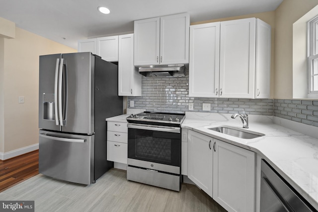 kitchen featuring appliances with stainless steel finishes, sink, light wood-type flooring, white cabinets, and light stone counters