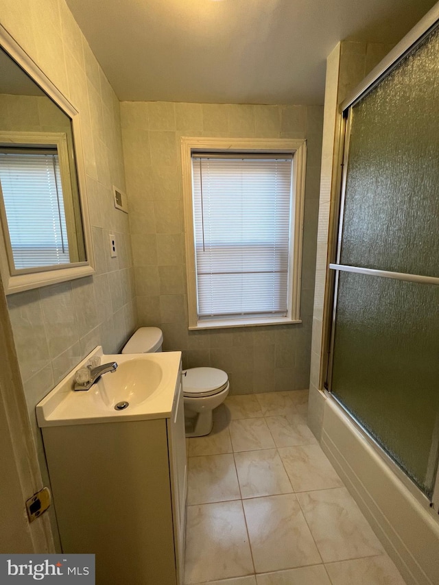 full bathroom with tile walls, toilet, tile floors, combined bath / shower with glass door, and vanity