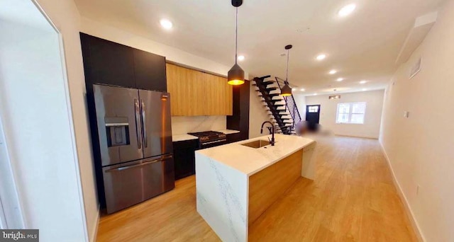 kitchen with an island with sink, stainless steel fridge with ice dispenser, light hardwood / wood-style flooring, hanging light fixtures, and sink