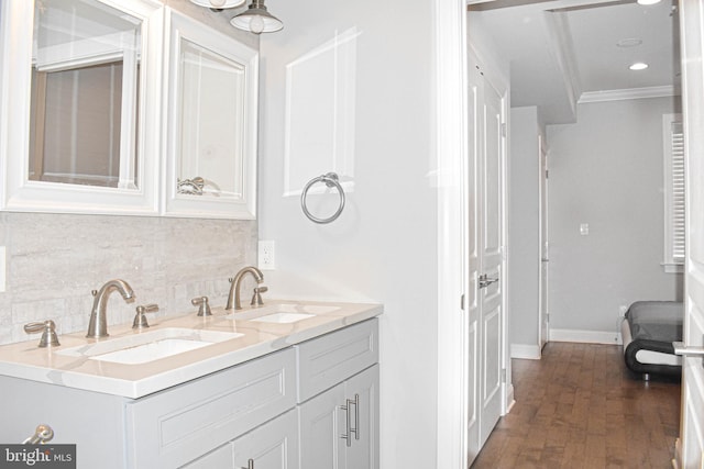 bathroom with double sink, crown molding, backsplash, wood-type flooring, and oversized vanity