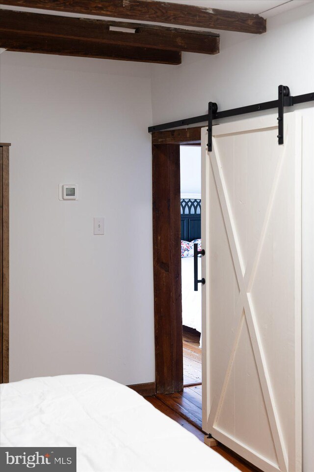 unfurnished bedroom featuring beam ceiling and a barn door