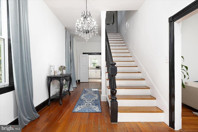 staircase with wood-type flooring and an inviting chandelier