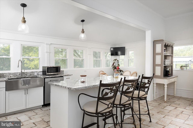 kitchen featuring white cabinets, hanging light fixtures, light stone countertops, appliances with stainless steel finishes, and a kitchen island