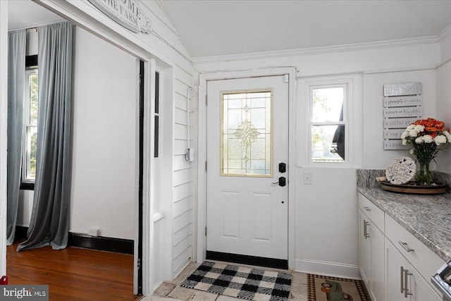 doorway with wood-type flooring, vaulted ceiling, and ornamental molding