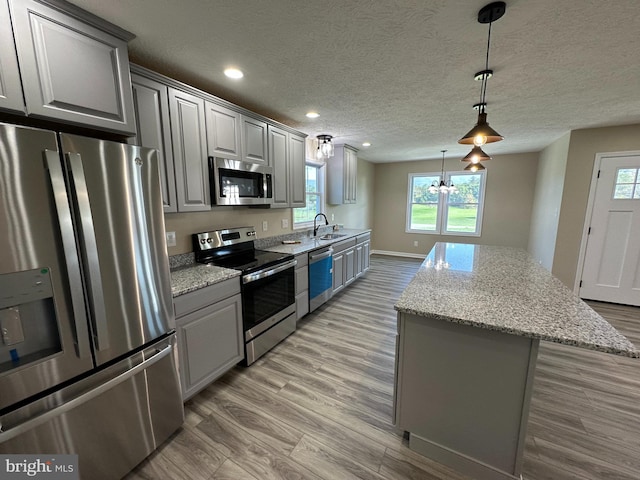 kitchen featuring appliances with stainless steel finishes, light stone counters, light hardwood / wood-style flooring, gray cabinets, and pendant lighting