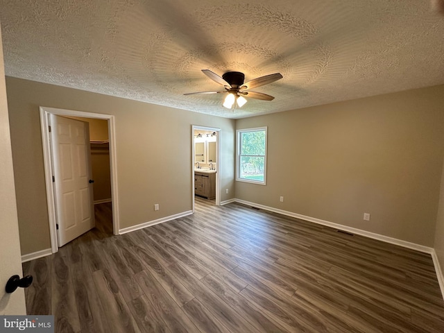 unfurnished bedroom with a closet, a walk in closet, ceiling fan, connected bathroom, and dark hardwood / wood-style flooring