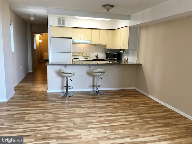 kitchen with a breakfast bar, white fridge, hardwood / wood-style flooring, stove, and kitchen peninsula