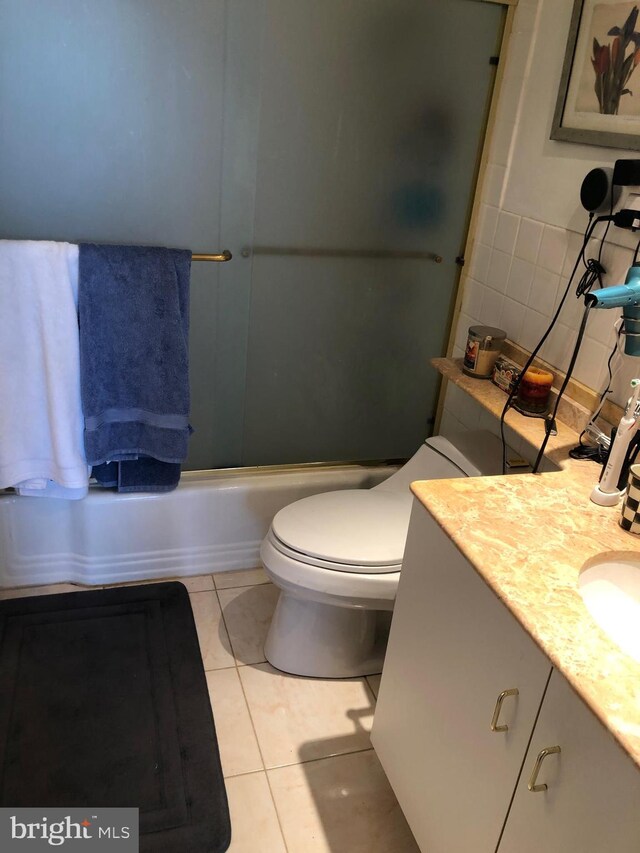 full bathroom featuring combined bath / shower with glass door, toilet, vanity, and tile flooring