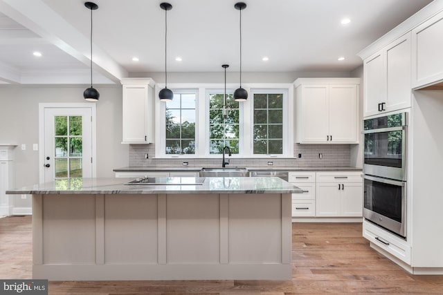 kitchen with white cabinets, a center island, light stone counters, and sink