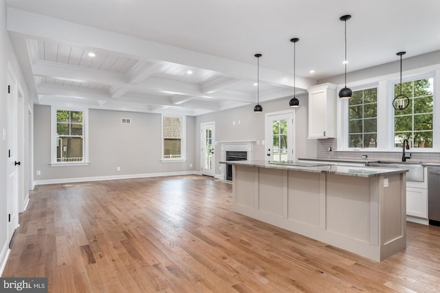 kitchen with white cabinetry, sink, light stone counters, a kitchen island, and light wood-type flooring